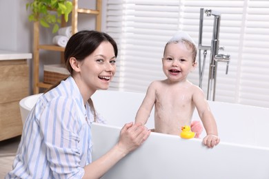 Mother bathing her cute little baby in tub at home