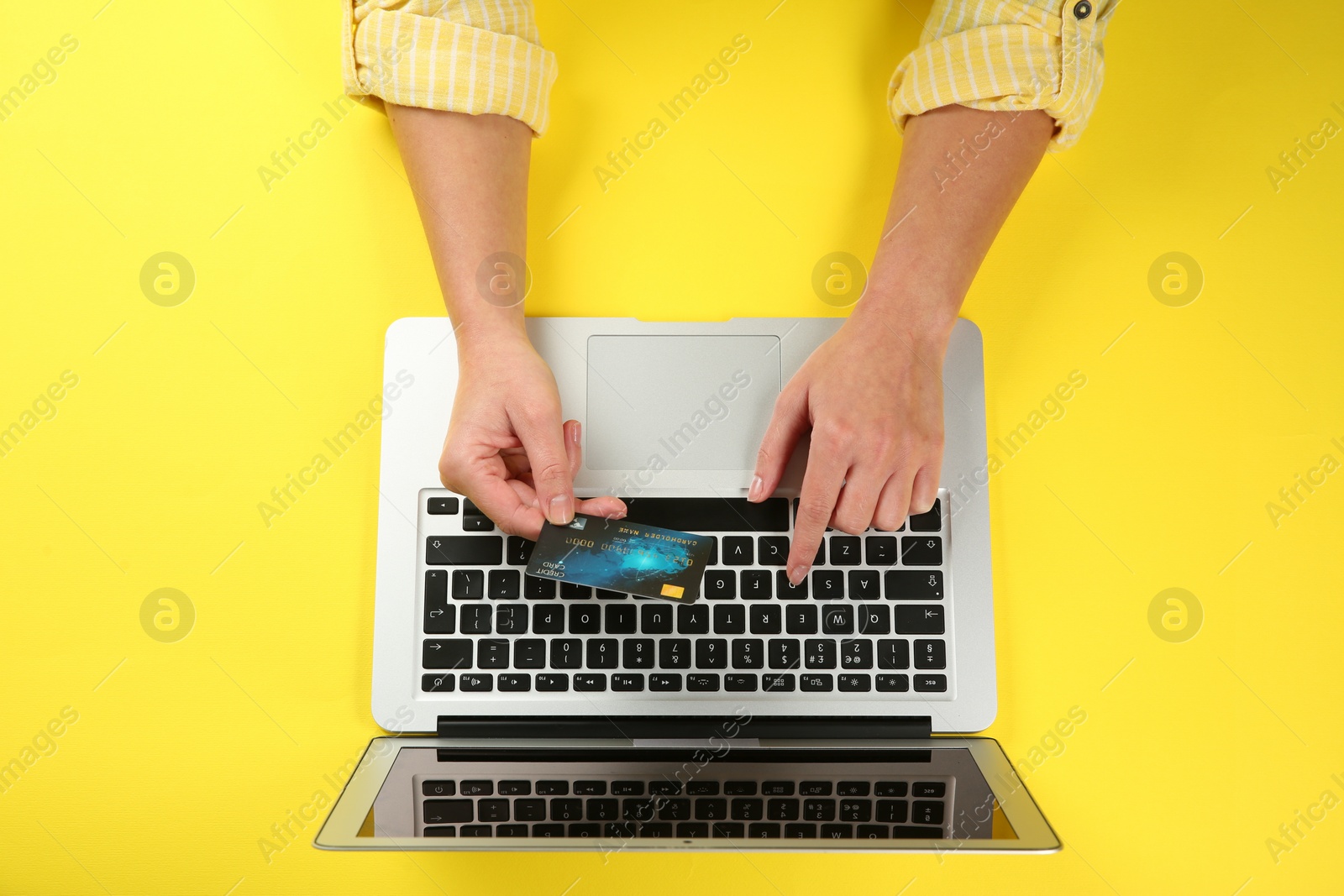 Photo of Online payment. Woman using credit card and laptop at yellow table, top view