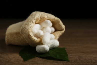 Photo of White silk cocoons with sackcloth bag and mulberry leaves on wooden table, closeup
