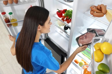 Young woman taking pack of meat out of refrigerator indoors, above view