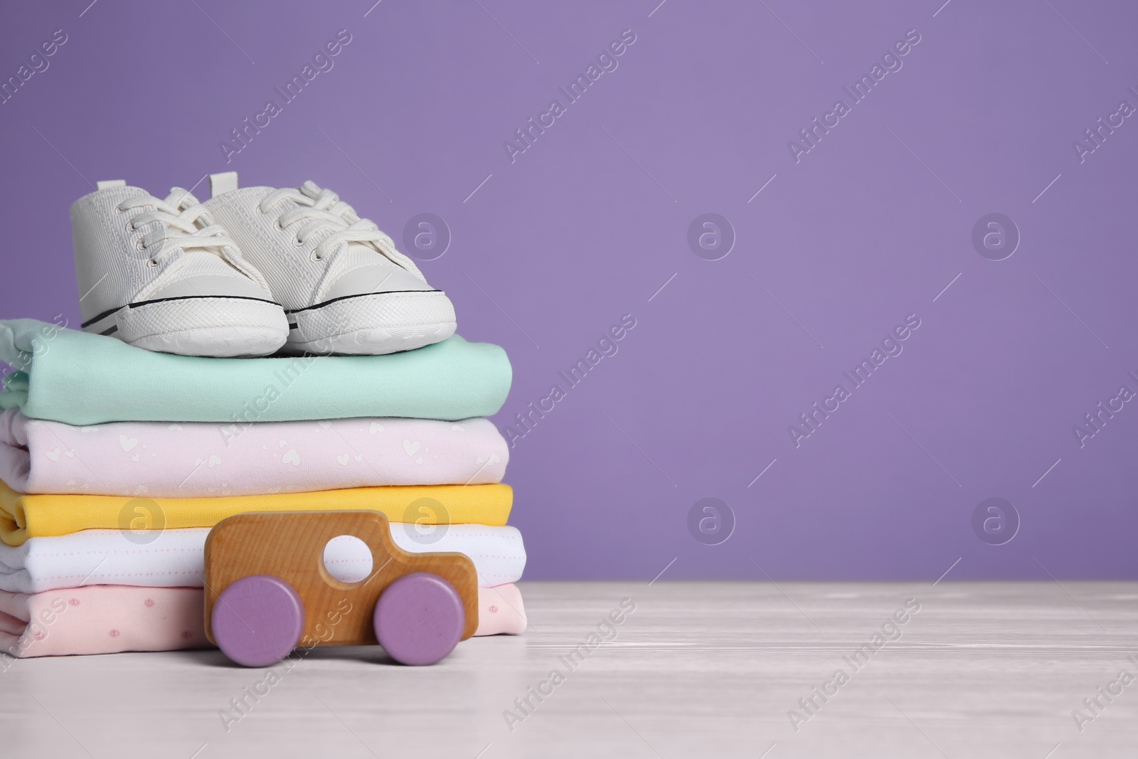 Photo of Children's shoes, stack of clothes and toy on white wooden table. Space for text