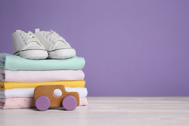 Children's shoes, stack of clothes and toy on white wooden table. Space for text