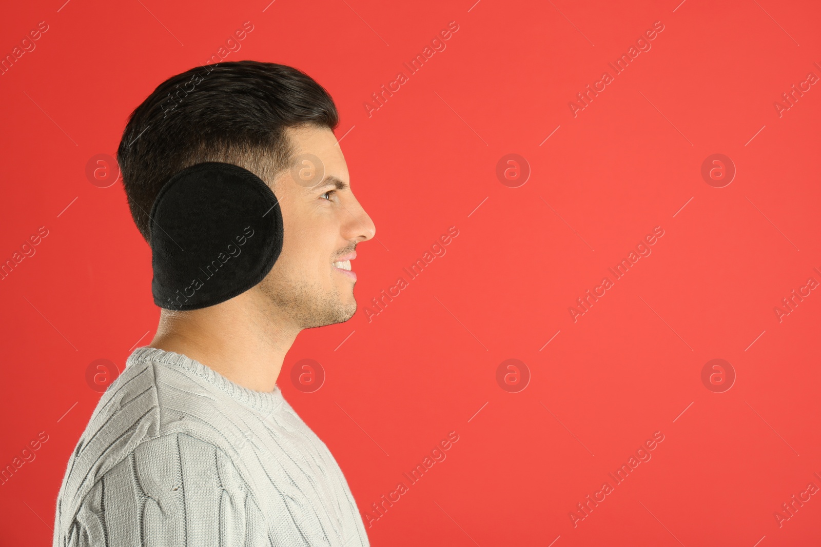 Photo of Man wearing stylish earmuffs on red background. Space for text