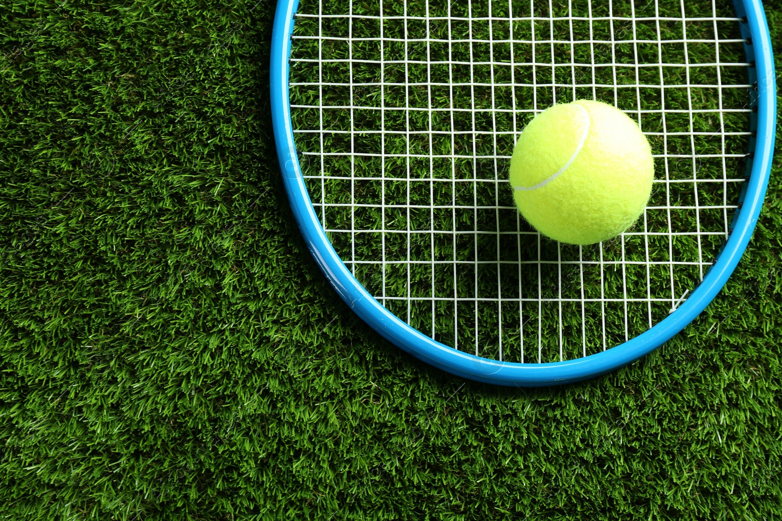 Photo of Tennis racket and ball on green grass, top view. Space for text