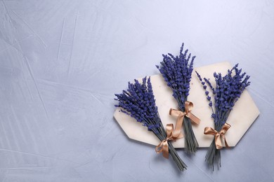 Photo of Bouquets of beautiful preserved lavender flowers and stone board on light grey textured table, top view. Space for text
