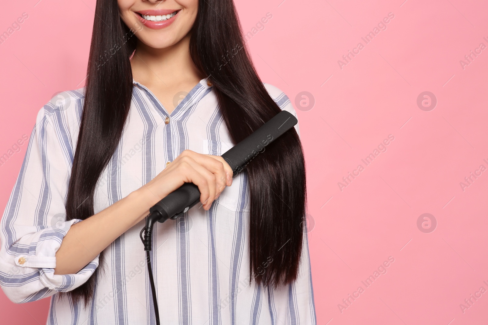 Photo of Happy woman using hair iron on pink background, closeup. Space for text