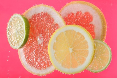 Photo of Slices of different citrus fruits in sparkling water on pink background