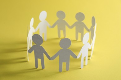 Photo of Teamwork concept. Paper figures of people holding hands on yellow background, closeup