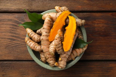 Photo of Bowl with fresh turmeric roots and leaves on wooden table, top view