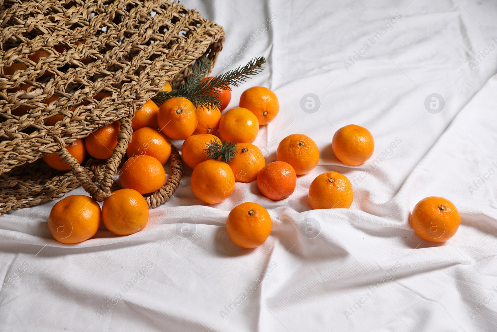 Photo of Stylish wicker bag with ripe tangerines on white bedsheet