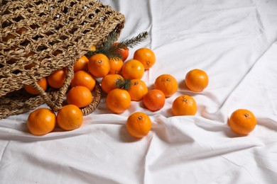 Photo of Stylish wicker bag with ripe tangerines on white bedsheet