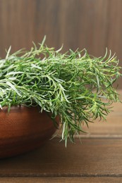 Photo of Bunch of fresh tarragon in bowl on wooden table