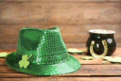 Green sequin hat, decorative clover leaves and pot of gold on wooden background, space for text. St Patrick's Day celebration