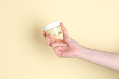 Woman holding jar of cream on yellow background, closeup. Space for text