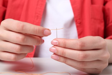 Photo of Woman inserting thread through eye of needle at table, closeup