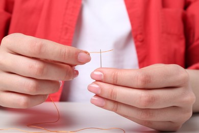 Woman inserting thread through eye of needle at table, closeup