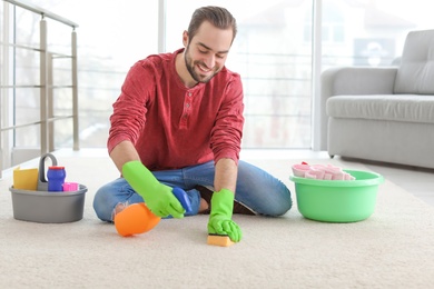 Young man cleaning carpet at home