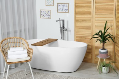 Photo of Stylish white tub and chair with towels in bathroom. Interior design