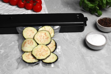 Photo of Sealer for vacuum packing and plastic bag with cut eggplant on light grey marble table