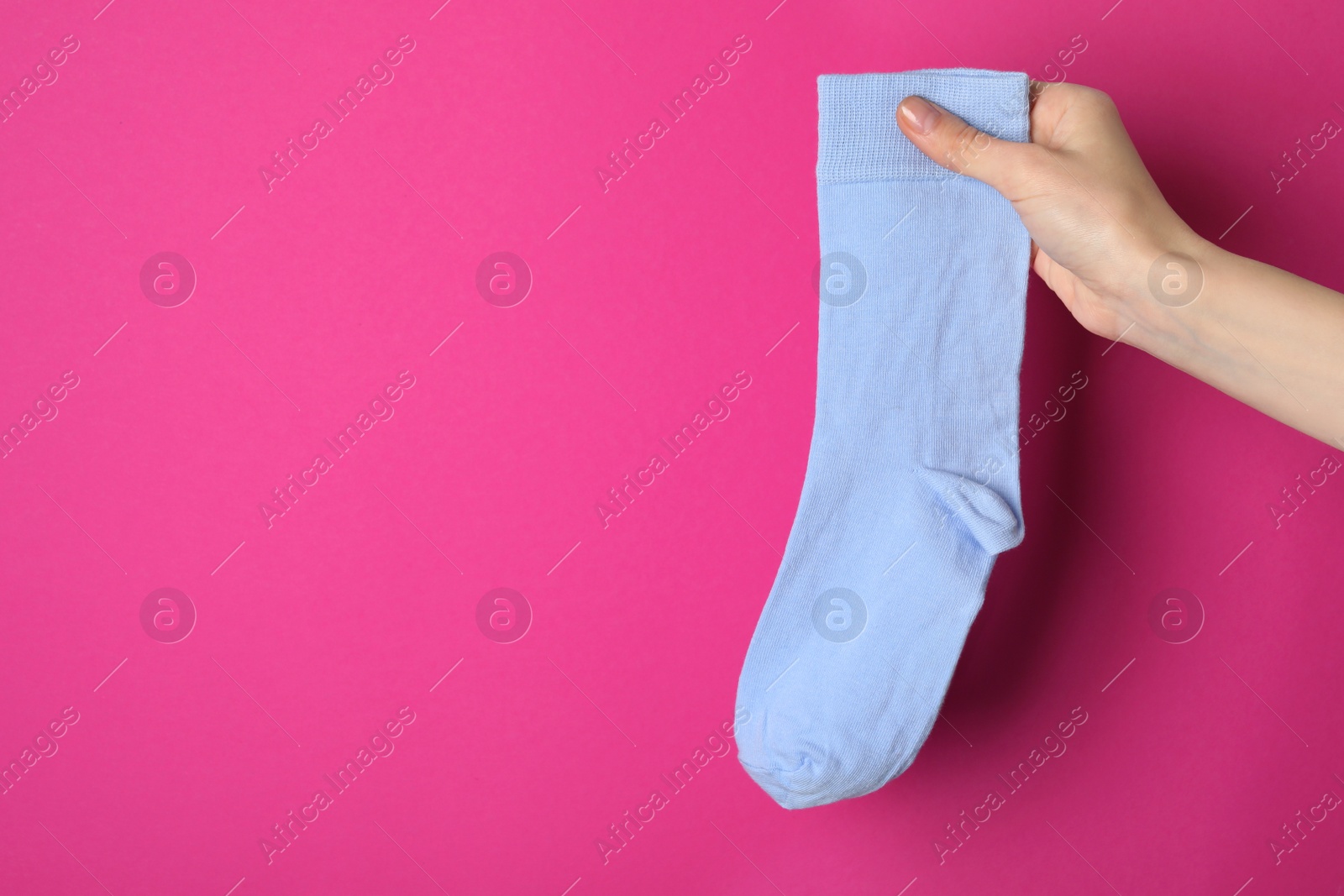 Photo of Woman holding pale light blue sock on bright pink background, closeup. Space for text