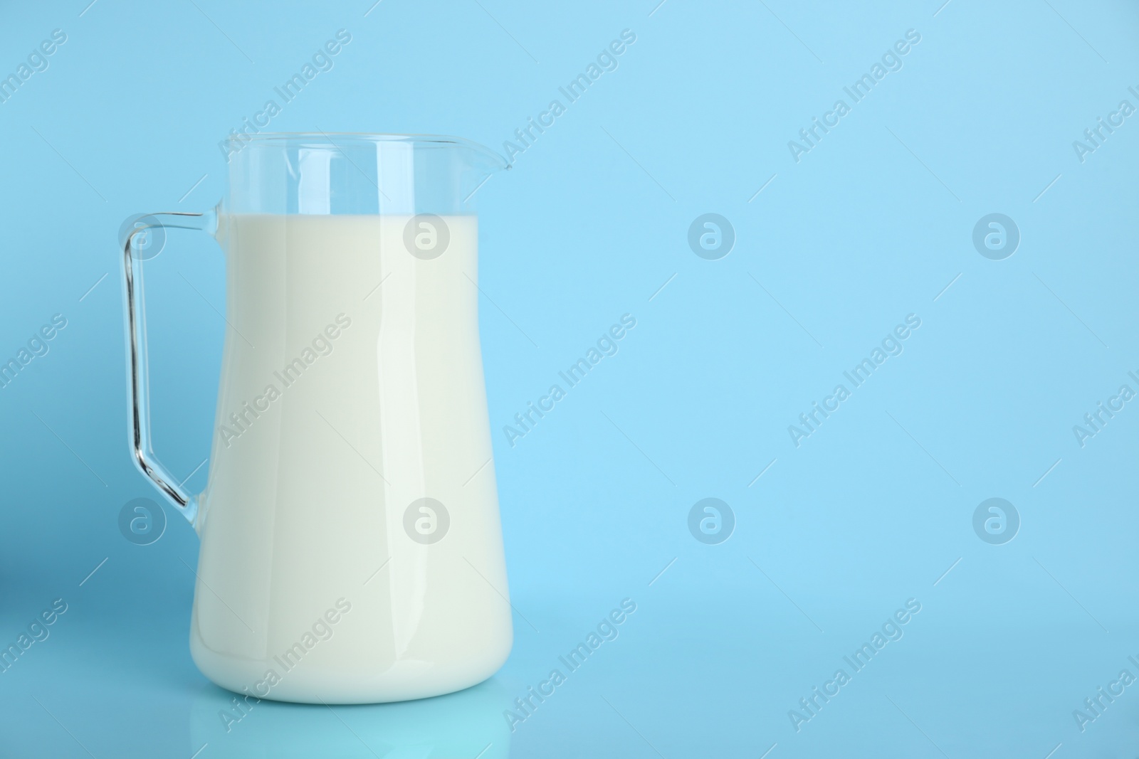 Photo of Jug of fresh milk on light blue background, space for text