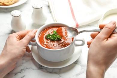 Photo of Woman eating fresh homemade tomato soup at marble table, closeup