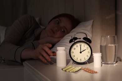 Photo of Young woman suffering from insomnia taking pill bottle in bed at night, focus on hand