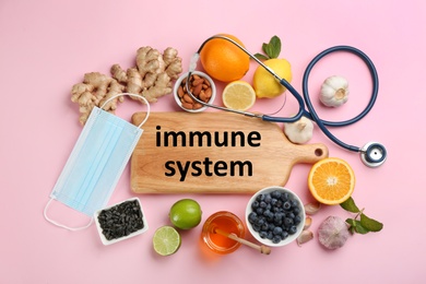 Photo of Board with phrase Immune System and natural products on pink background, flat lay