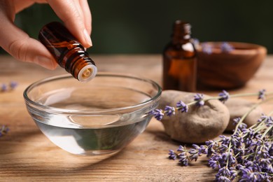 Photo of Woman dripping lavender essential oil from bottle into bowl at wooden table, closeup. Space for text