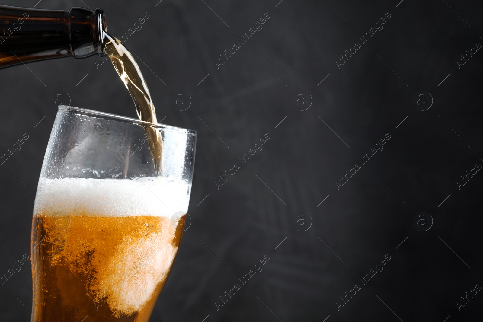 Photo of Pouring cold tasty beer from bottle into glass on black background, closeup. Space for text