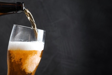 Photo of Pouring cold tasty beer from bottle into glass on black background, closeup. Space for text