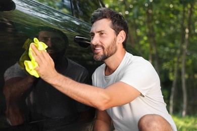Photo of Happy man washing car door with rag outdoors