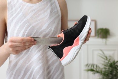 Woman putting orthopedic insole into shoe indoors, closeup. Foot care