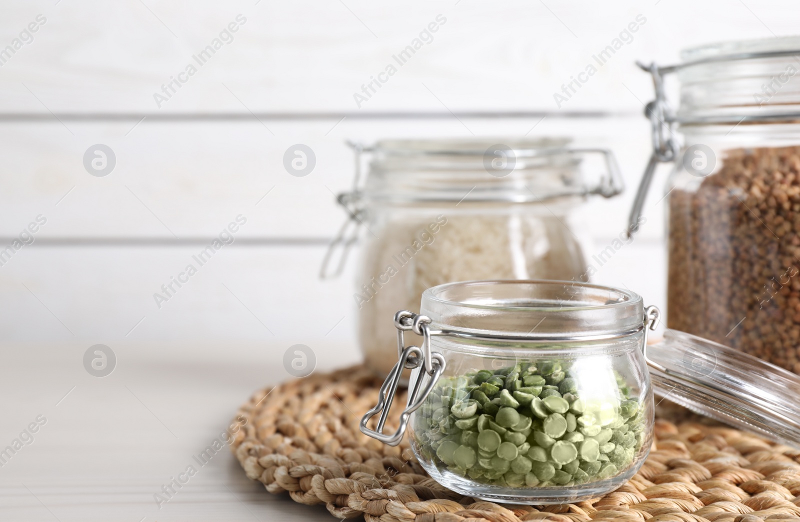 Photo of Dry peas and groats in jars on white table. Space for text