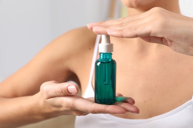 Photo of Woman with bottle of cosmetic serum on blurred background, closeup