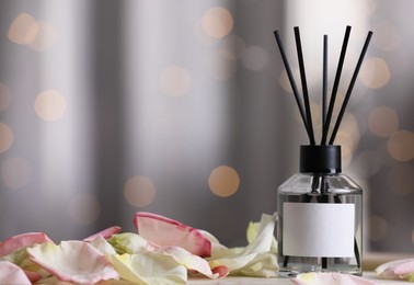 Photo of Aromatic reed air freshener and petals on table against blurred background, space for text