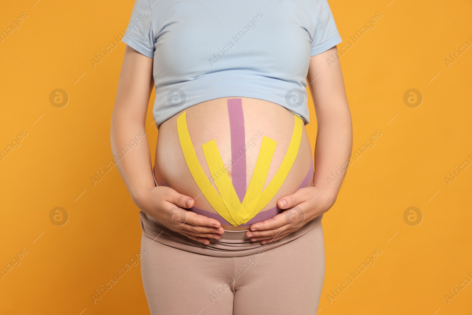 Photo of Pregnant woman with kinesio tapes on her belly against orange background, closeup