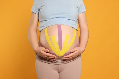 Pregnant woman with kinesio tapes on her belly against orange background, closeup