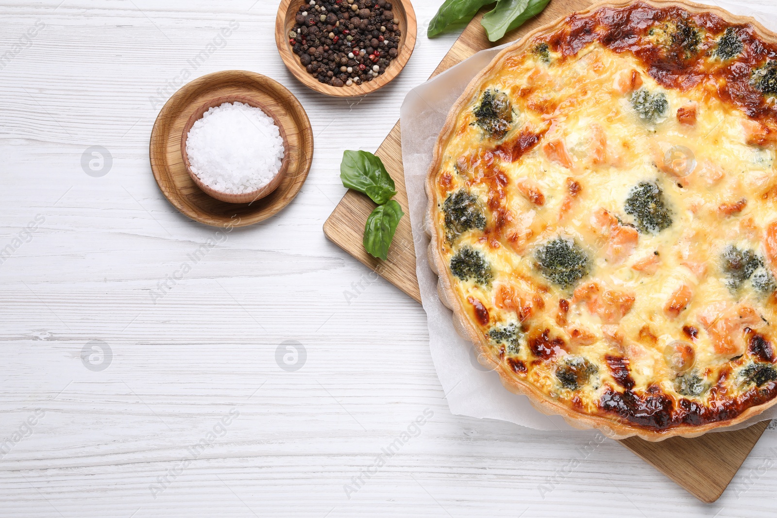Photo of Delicious homemade quiche with salmon, broccoli, basil leaves and spices on wooden table, flat lay. Space for text