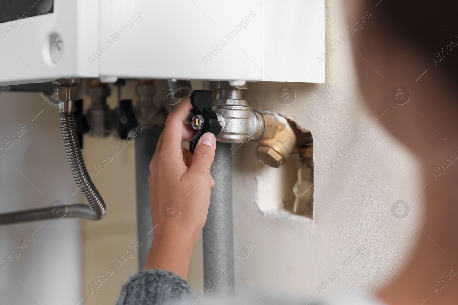 Photo of Woman turning on valve of gas boiler indoors, closeup