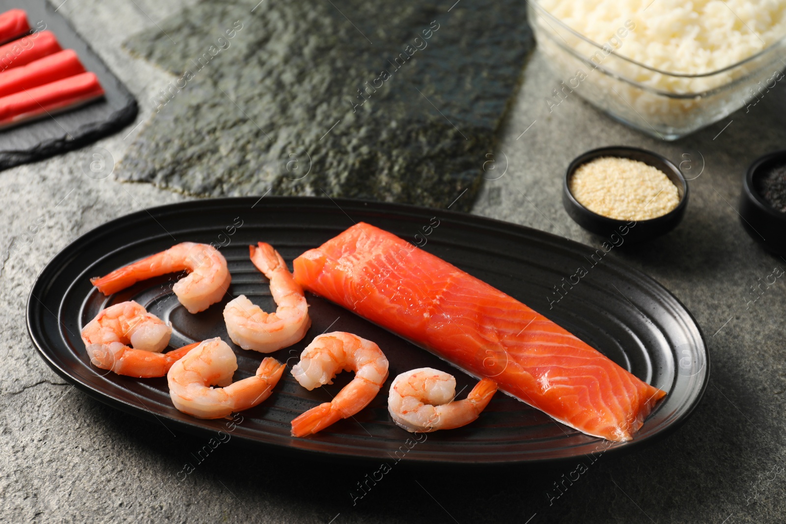 Photo of Fresh salmon, shrimps and other ingredients for sushi on dark textured table, above view