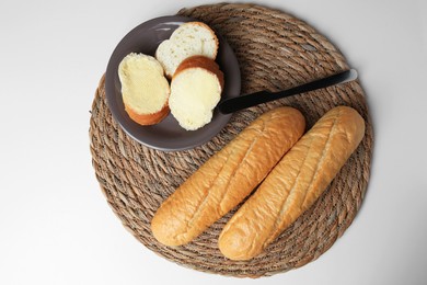 Photo of Whole and cut baguettes with fresh butter on white table, top view