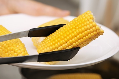 Photo of Taking corn cob from plate with tongs, closeup