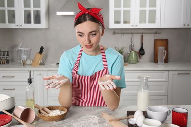 Photo of Exhausted woman with dirty hands in messy kitchen. Many dishware, utensils and scattered flour on countertop