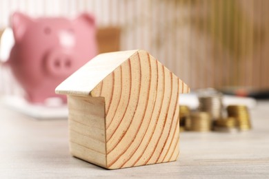 Photo of House model, stacked coins and piggy bank on wooden table, selective focus