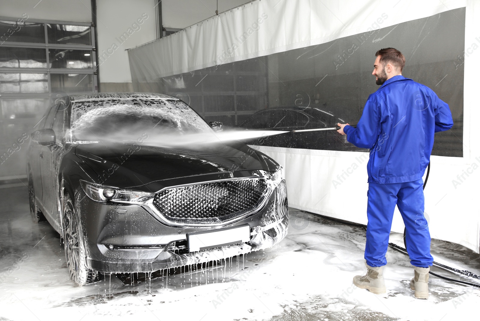 Photo of Worker cleaning automobile with high pressure water jet at car wash