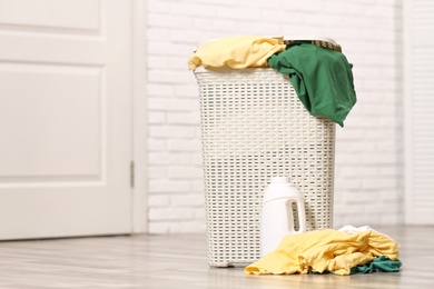 Photo of Laundry basket with dirty clothes and detergent on floor in room, space for text