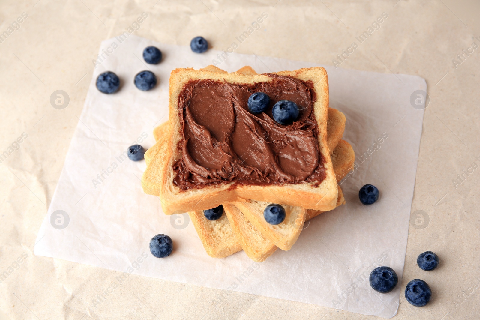 Photo of Tasty toast with chocolate paste and blueberries on parchment paper, above view