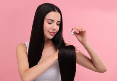 Photo of Beautiful woman applying hair serum on pink background. Cosmetic product