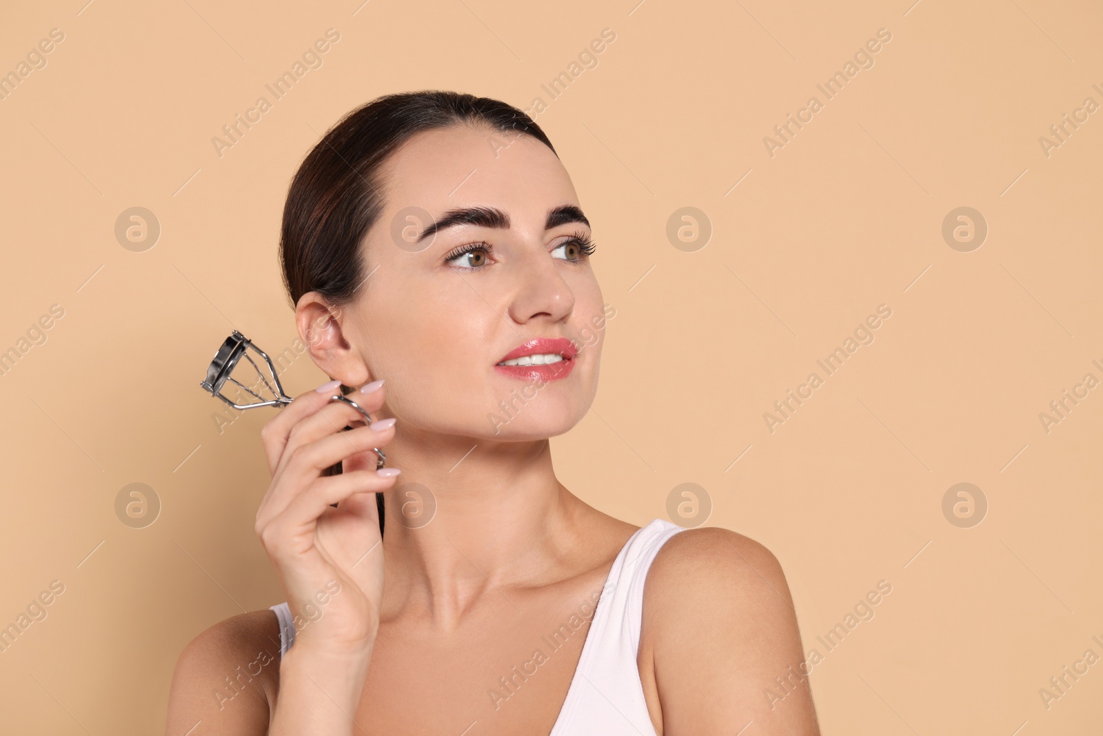 Photo of Woman with eyelash curler on beige background. Space for text